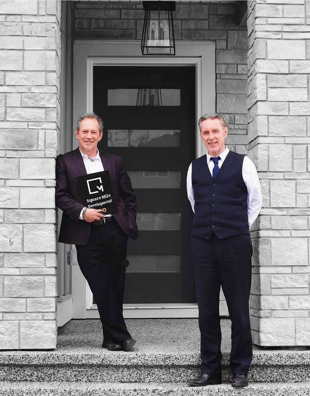 Two Square Mile principals at the front door of a completed home, holding the Square Mile Development portfolio
